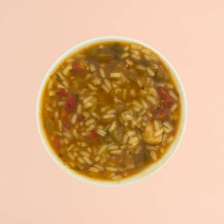 Top view of a bowl of gumbo with meats, rice and vegetables in a broth atop a pink stone table top.の写真素材