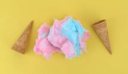 Pink and blue cotton candy between two ice cream sugar cones atop a yellow background.