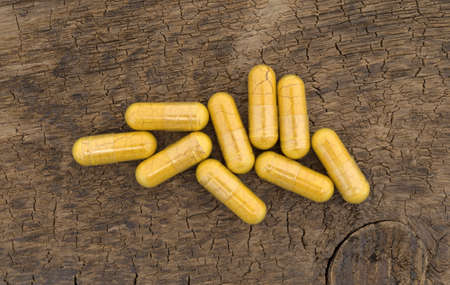 Top view of a group of turmeric capsules on an old brown wood board.