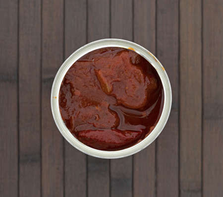 Top view of an opened can of chipotle peppers in an adobo sauce atop a brown wood place mat.の写真素材