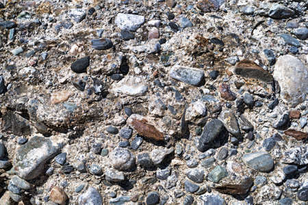 Close view of a very worn and weathered concrete wall with rocks protruding from the masonry.