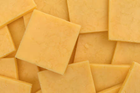 Top close view of several square slices of gouda cheese.