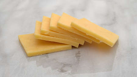 Side view of several square slices of gouda cheese on a gray marble cutting board.の写真素材