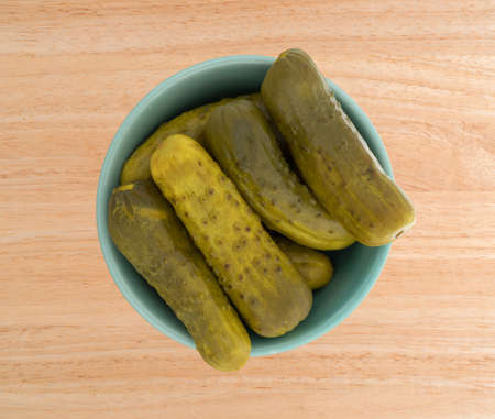 Top view of a bowl filled with kosher baby dill pickles on a wood table top.の写真素材