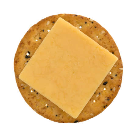 A square slice of gouda cheese on a round multi grain cracker isolated on a white background