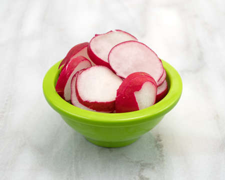 Several slices of radish in a green bowl atop a gray marble counter top.の写真素材