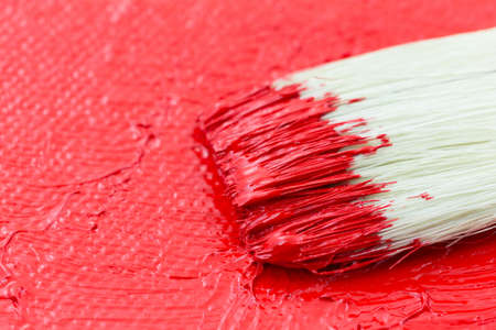 Close view of wet red paint on an artist canvas with a brush.の写真素材