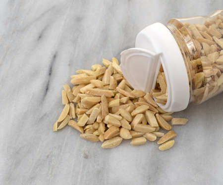 Slivered almonds spilling from a plastic container onto a marble counter top.の写真素材