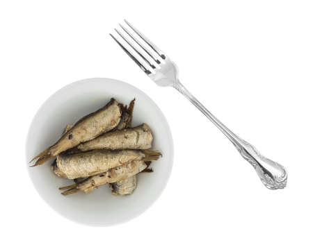 Top view of canned smoked sprats in a small bowl with a fork to the side isolated on a white background.の写真素材