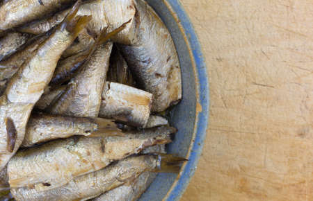 Top close view of canned smoked sprats in a stoneware bowl on an old worn cutting board.の写真素材