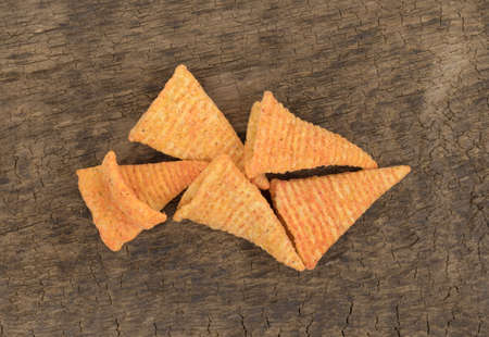 Top view of a small serving of cheese flavored cone shaped corn chips on an old brown board.の写真素材