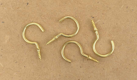 Top view of four large brass cup hooks atop a brown pressed board.の写真素材