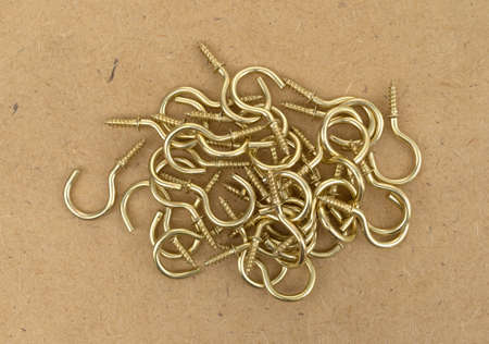 Top view of a jumble of large brass cup hooks atop a brown pressed board.の写真素材