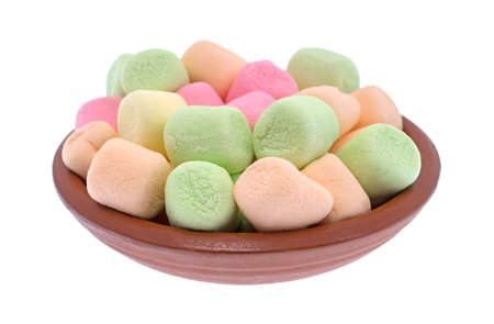 A small red clay bowl filled with colorful pastel hued miniature green, pink, yellow and orange marshmallows isolated on a white background.の写真素材