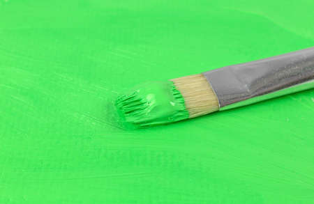 Close view of wet green acrylic paint on a brush atop a painted heavyweight artist paper.の写真素材