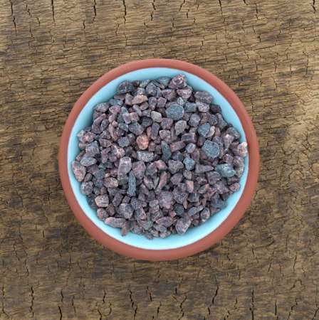Top view of a small terracotta bowl of Himalayan black salt on an old wood brown board.の写真素材