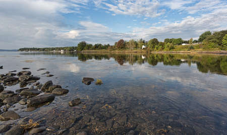 View of the coastline at Searsport, Maine in the summertime with water reflections near the rocky shore and blue sky with clouds above.の写真素材