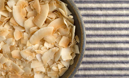 Top close view of a stoneware bowl filled with toasted coconut flakes on a blue and white striped...