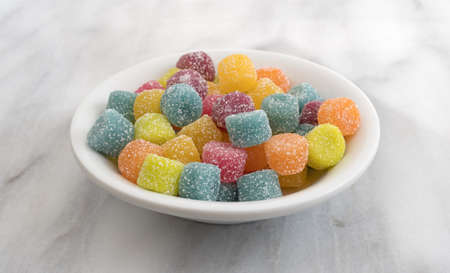 A small white bowl filled with sugar coated gummy candy on a gray marble counter top.