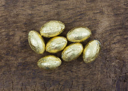 Top view of several pieces of gold foil wrapped chocolate Easter candy eggs on an old wood board.の写真素材