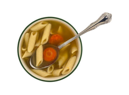 Top view of a small bowl filled with penne pasta, carrots and celery soup in a chicken broth plus a spoon in the food isolated on a white background.の写真素材