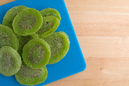 Top view of several slices of glazed kiwi fruit on a blue plastic cutting board atop a wood counter top.の写真素材