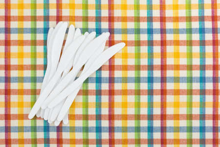Top view of a group of white plastic knives on a colorful tablecloth.の写真素材