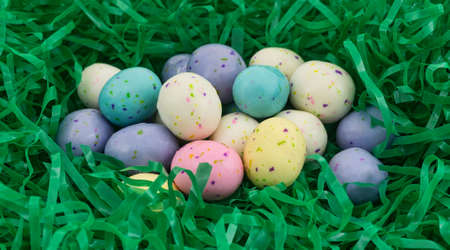 A group of speckled Easter egg malt ball candies nestled in a green plastic grass.