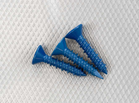 Top view of three concrete anchor screws on a gray plastic background.