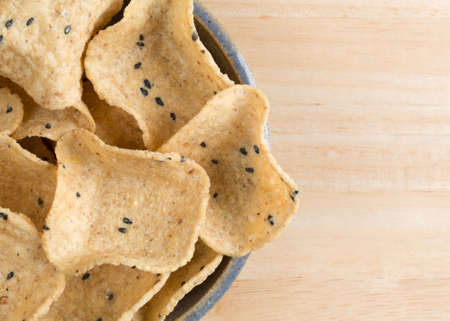 Top close view of a bowl filled with corn tortilla dipping shells on a wood table top.