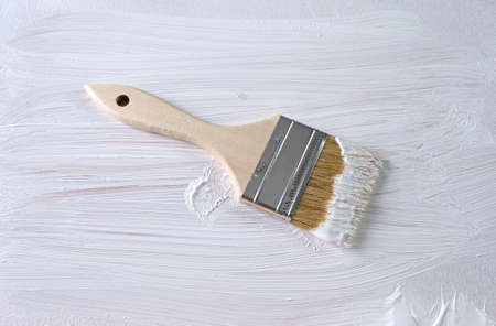 Top view of a wet paintbrush atop a white painted surface.