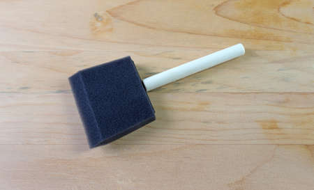 A new black foam paintbrush atop old pine boards that are stained and grungy.