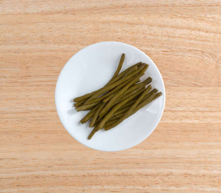 Top view of a serving of marinated gourmet green beans on a white plate atop a wood table top.