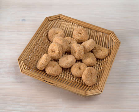 Small bite size caramel flake donuts in a wood wicker basket atop a whitewashed pine tabletop.