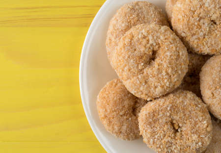 Top close view of caramel flake donuts on a white plate atop a bright yellow painted wood table.