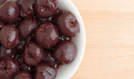 Top close view of a small white bowl of sweet pitted cherries on a wood table.
