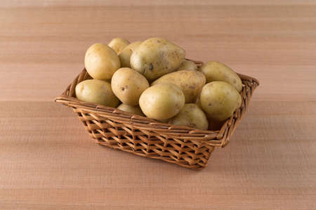 A small wicker basket filled with gold baby potatoes on a cedar counter top.の写真素材