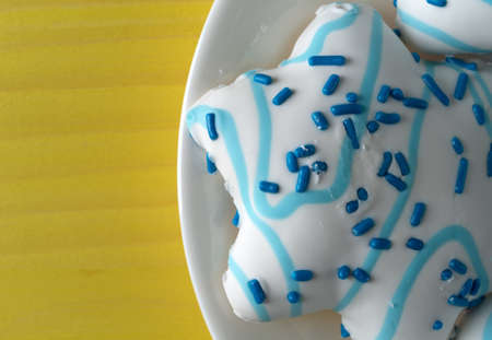 Top close view of large blue and white decorated star shaped Christmas cookies on a white plate atop a yellow painted table top.の写真素材