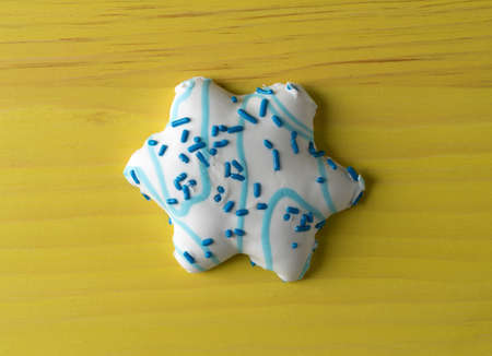 A large blue and white decorated star shaped Christmas cookie on a yellow painted table top.