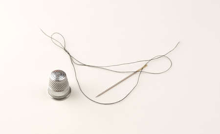 An old metal sewing thimble and long threaded needle with string on white paper.