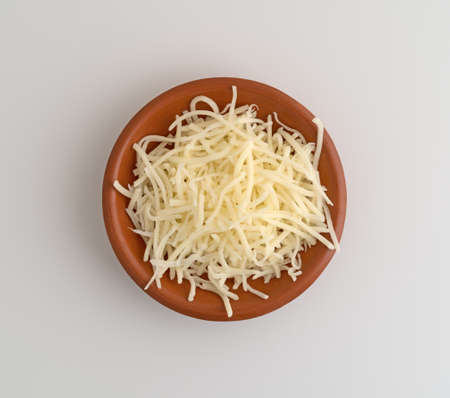 Top view of a small bowl filled with sharp white cheddar cheese atop white table.