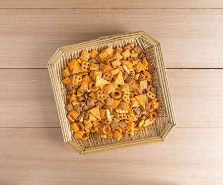 Top view of a mix of small snack food in a wicker basket on a wood table top.の写真素材