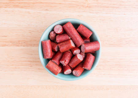 Top view of a green bowl filled with bite size beef sausages on a wood table top.