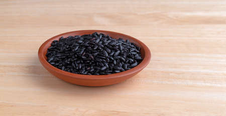 A small bowl filled with organic black rice isolated on a wood table.の写真素材