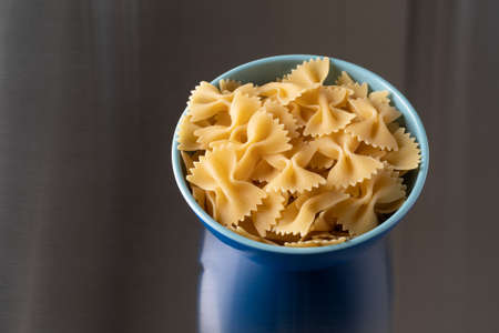 A blue bowl filled with bow tie pasta isolated on a steel counter top illuminated with natural light.の写真素材