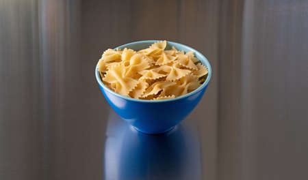 Side view of a blue bowl filled with bow tie pasta isolated on a steel counter top illuminated with natural light.の写真素材
