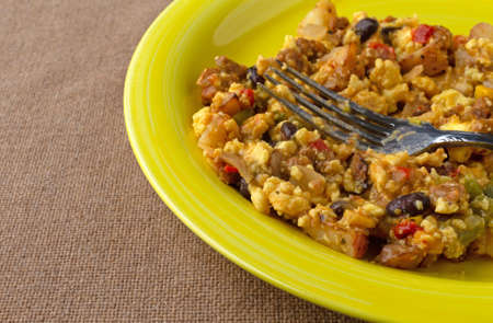 A scrambled egg burrito meal on a yellow plate with a fork atop a brown tablecloth.の写真素材