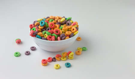 A bowl filled with generic sugar coated fruity flavored breakfast cereal with milk and spilled cereal on a table.の写真素材