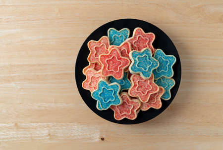 Top view of several star shaped sugar cookies with blue and red sprinkles on a black dish atop a wood table top.の写真素材