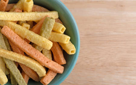 Top close view of a green bowl filled veggie straws on a wood table.